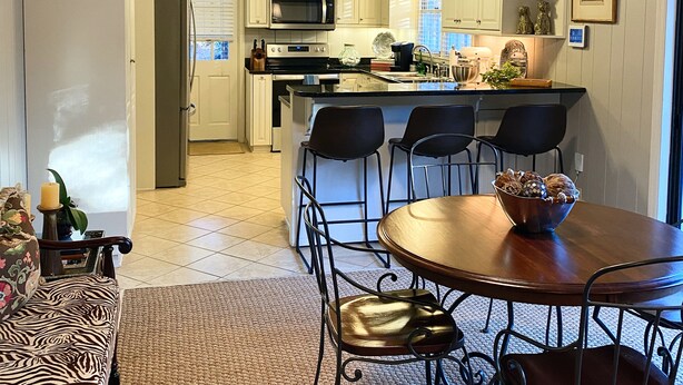 Een kleine keuken met witte kastjes, een magnetron, en een eethoek met een houten tafel en metalen stoelen.