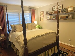 A four-poster bed with a white bedspread, a bedside table with a lamp, and a wall with framed pictures and bookshelves. - Perfect Masters rental less than 2 miles from the course! (Augusta)