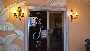Entrada de un spa con puerta de vidrio, dos luces fijadas a la pared y un mural grande con motivos de hojas.