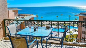 Un balcón con mesa y sillas que da a una piscina y vistas al océano.