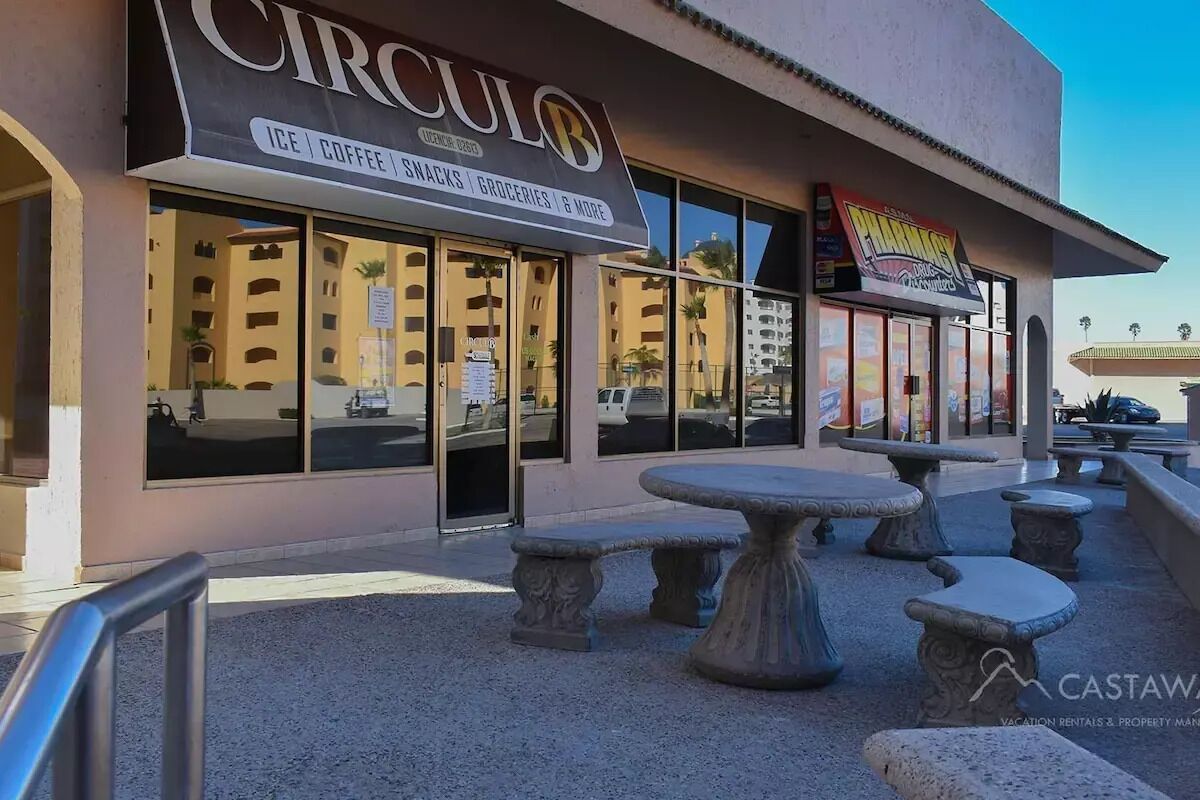 A building with a sign for 'CIRCUO' offering ice, coffee, snacks, groceries, and more. There are outdoor stone tables and benches.