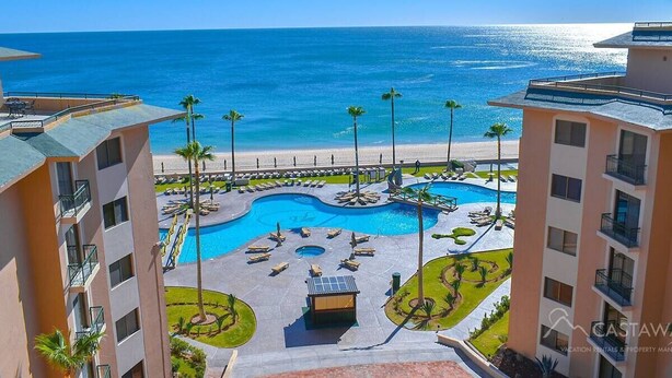 Un resort con piscina central, palmeras y vistas a la playa.