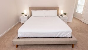 A neatly arranged bedroom with a large bed, two bedside tables with lamps, and a window with blinds. - New! Modern Large House Great Location near UNC-Charlotte, TopGolf, Carowinds (Charlotte)
