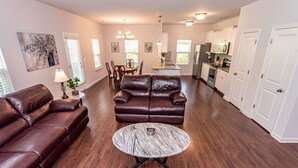A spacious living room with a brown leather sofa, a marble coffee table, and a dining area with a chandelier. - New! Modern Large House Great Location near UNC-Charlotte, TopGolf, Carowinds (Charlotte)