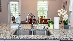 A kitchen with a granite countertop, stainless steel sink, and a double faucet. There are chairs, a table, and a potted orchid. - New! Modern Large House Great Location near UNC-Charlotte, TopGolf, Carowinds (Charlotte)