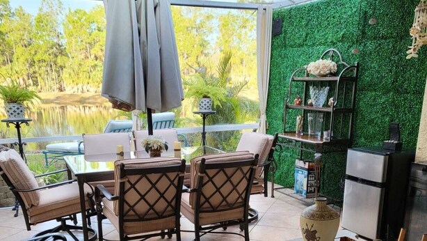Un patio con mesa y sillas, un estante pequeño con adornos, y vista a un paisaje natural a través de un ventanal.