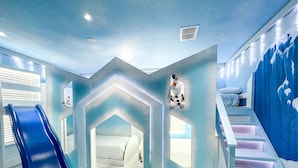 A children's playroom with a blue slide, a small bed, and a wall-mounted snowman decoration.
