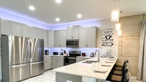 A modern kitchen with stainless steel appliances, a marble-tiled floor, and a bar area with stools.
