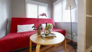 Une pièce avec un canapé rouge, une table ronde en bois sur laquelle se trouvent une bouteille et des verres, et un lampadaire.