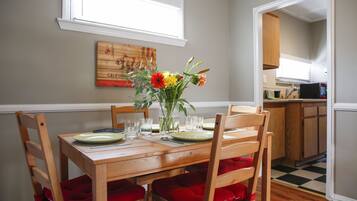 Un comedor con una mesa de madera, sillas con cojines rojos, un florero con flores y un cuadro en la pared.