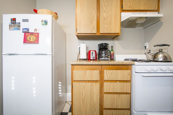 A compact kitchen with a white refrigerator, wooden cabinets, a gas stove, a coffee maker, and a toaster.