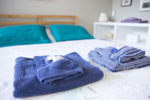 Una cama bien hecha con toallas azules y una colcha blanca.