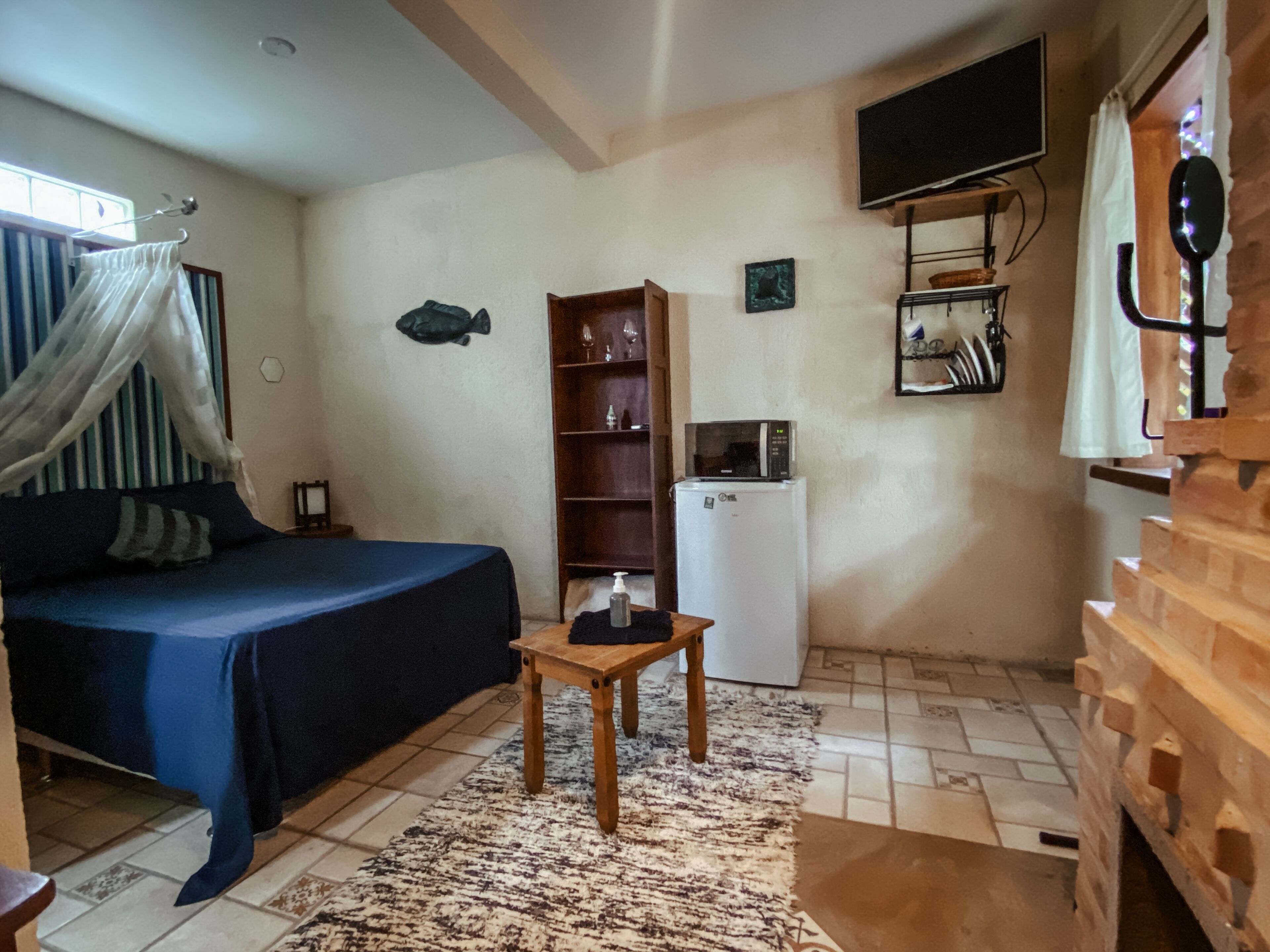 Un dormitorio con cama, una mesita, un armario, televisor y refrigerador.
