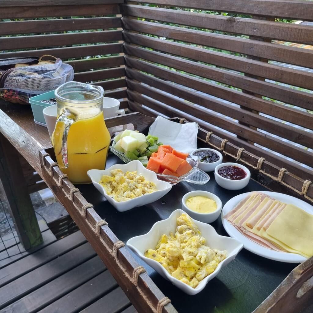 A breakfast tray with a pitcher of orange juice, scrambled eggs, ham, cheese, and fresh fruit on a wooden bench.