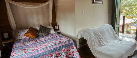 A bedroom with a canopy bed, a bedside table, a chair, and a balcony with a view.