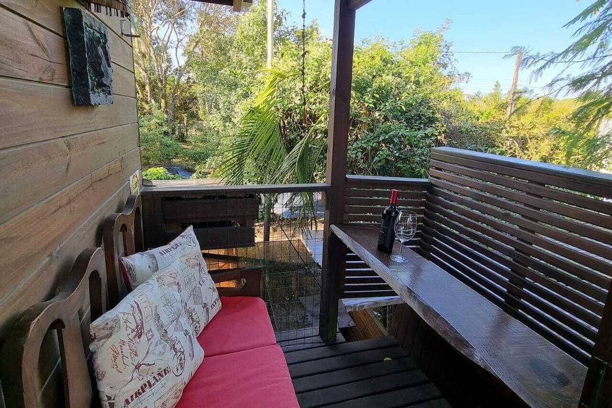 Eine Holzterrasse mit einer roten gepolsterten Bank und einem Holztisch mit Flasche und Glas.