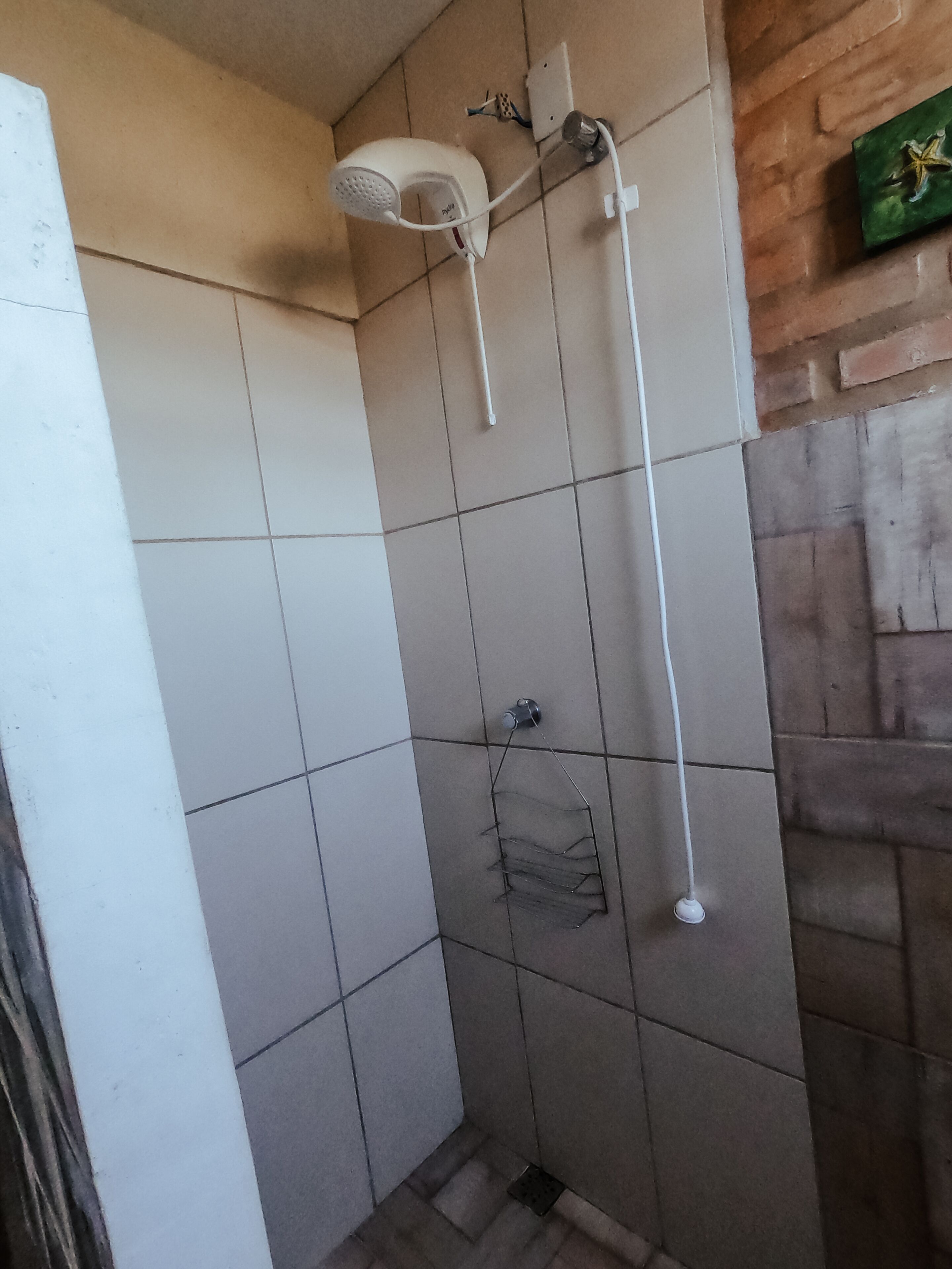 Ein kleiner Duschbereich mit Fliesen, einer Handbrause und einem am Wand montierten Wasserhahn.