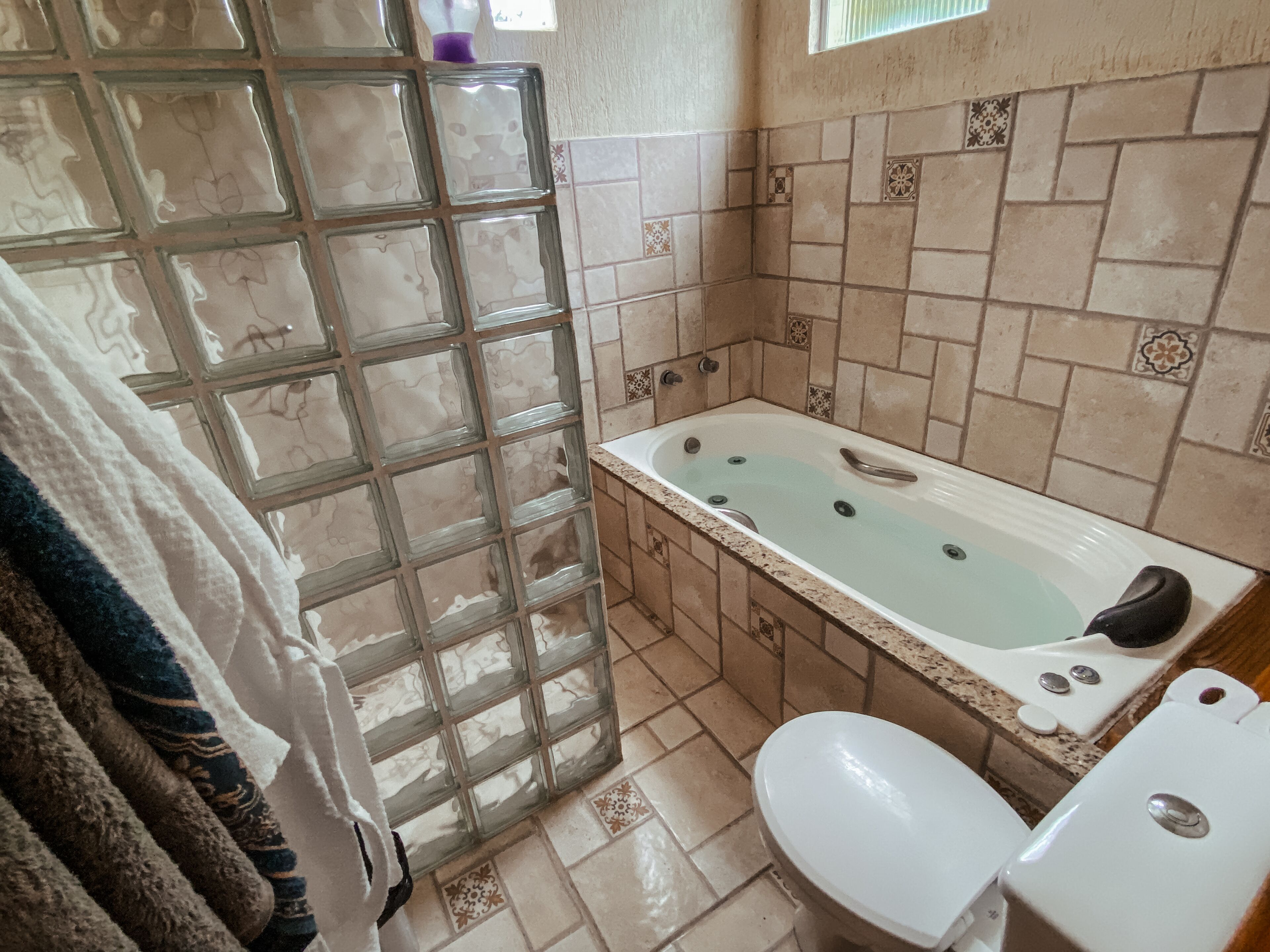 A bathroom with a glass shower enclosure, a bathtub, a toilet, and tiled walls.
