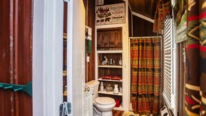 A compact bathroom with a toilet, shelves, and a shower curtain. - Yowie Cabin (Benton)