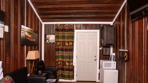 A room with a couch, a coffee table, a lamp, a television, a microwave, and a patterned curtain. - Yowie Cabin (Benton)