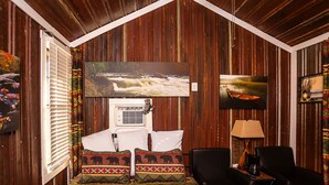 A room with a bed, two chairs, a TV, and a window with blinds. - Yowie Cabin (Benton)