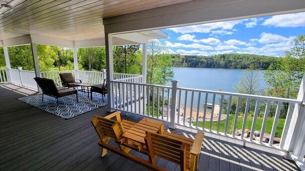 Una terraza cubierta con un banco y sillas de madera, una mesa y vistas a un lago.