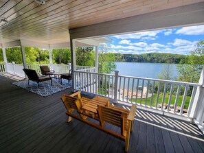 Une terrasse couverte avec un banc et des chaises en bois, une table et une vue sur un lac.