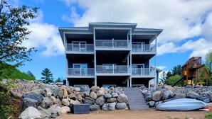 Un edificio de varios pisos con balcones y una terraza de madera que da a un estanque con rocas y un kayak.