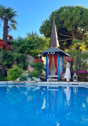 A pool area with a gazebo, palm trees, and various plants. - Milton Boutique Hotel (Jesolo)