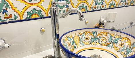 A bathroom with a decorative tile backsplash, a sink with a blue and yellow bowl, a silver faucet, and a silver-handled brush on the counter.