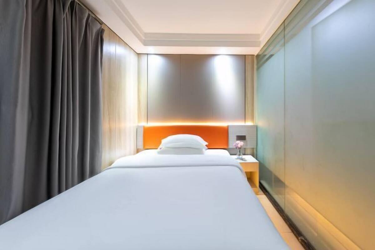 A hotel room with a bed, a nightstand, a lamp, and a wall-mounted light fixture.