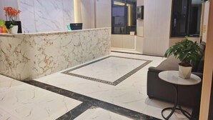 A lobby with a marble reception desk, a sofa, a small table with a plant, and a patterned floor design. - Alice Hotel (Guangzhou Olympic Sports Chebei Subway Station Branch) (Guangzhou)