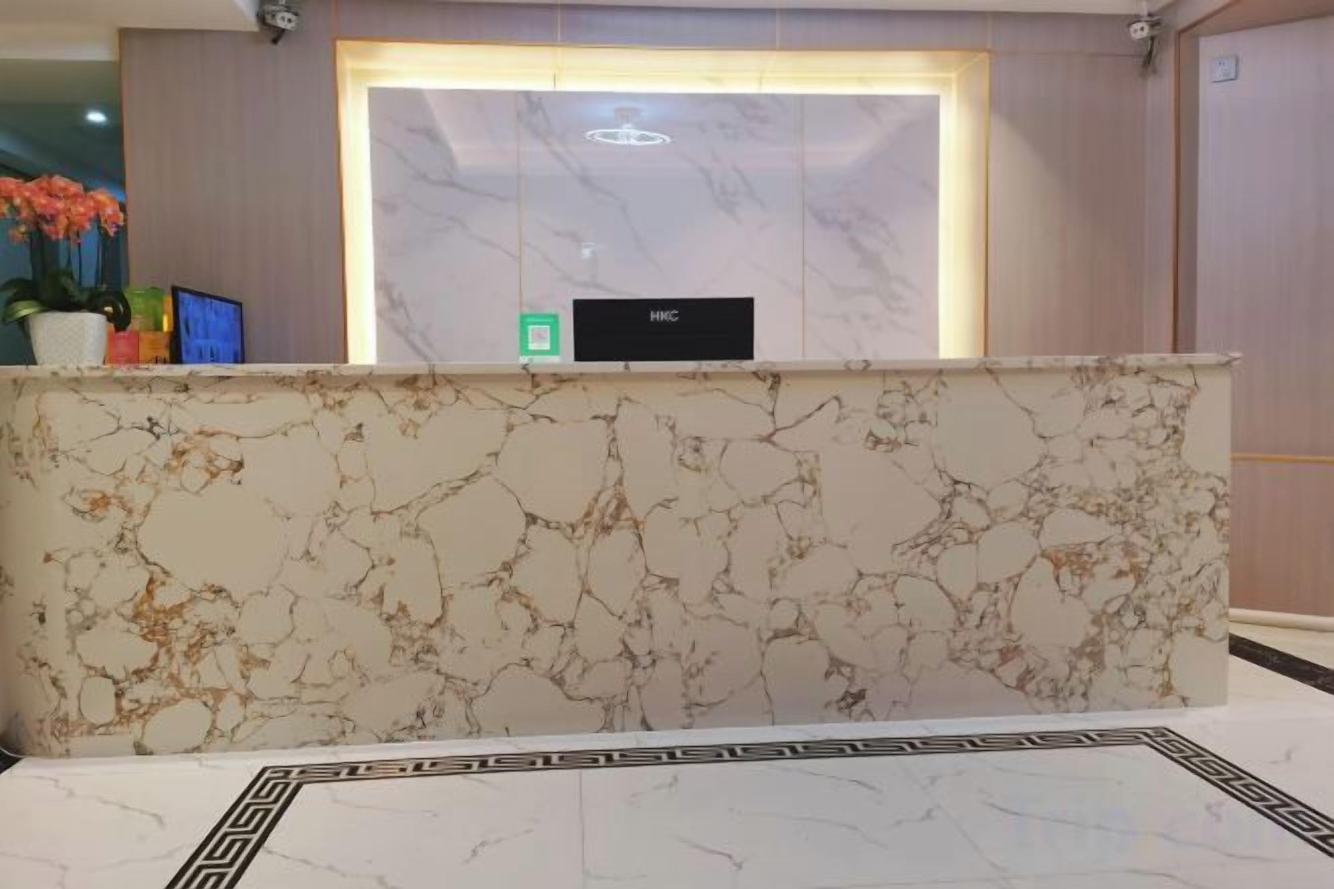 A reception desk with a marble top, a reception area with a marble wall, and a small potted plant on the left.
