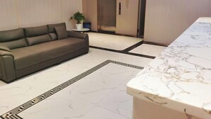 A modern lobby with a grey sofa, a marble reception desk, and an elevator. - Alice Hotel (Guangzhou Olympic Sports Chebei Subway Station Branch) (Guangzhou)