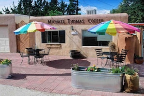 A small outdoor seating area with tables and chairs, a colorful umbrella, and a sign reading "Michael Thomas Coffee". - Bright and centrally located with enclosed yard, pets welcome (Albuquerque)