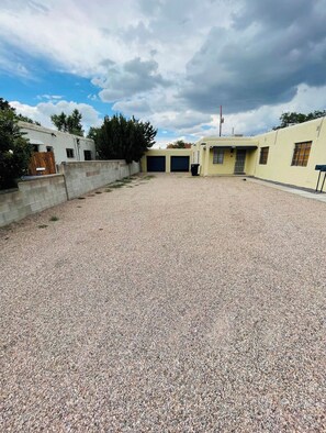 Outdoor space with a gravel surface, bordered by a building with a flat roof and parking spaces.
