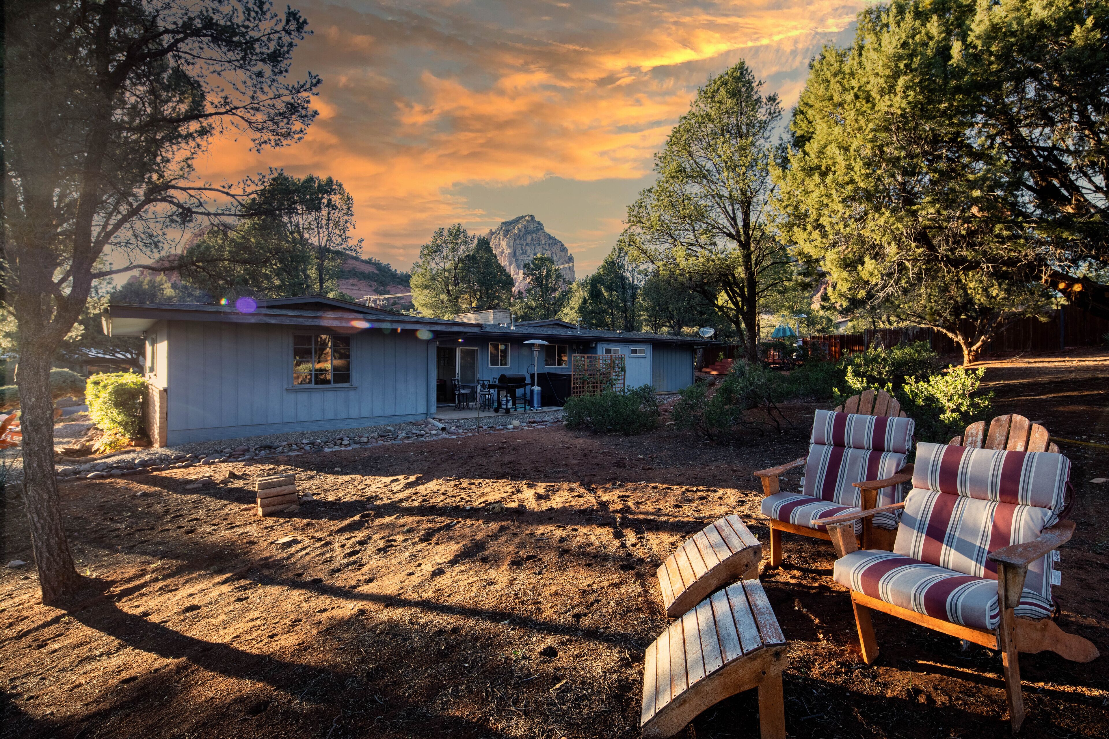 Una casa con un patio que incluye dos sillas Adirondack, una mesita y un espacio de estar techado al aire libre.