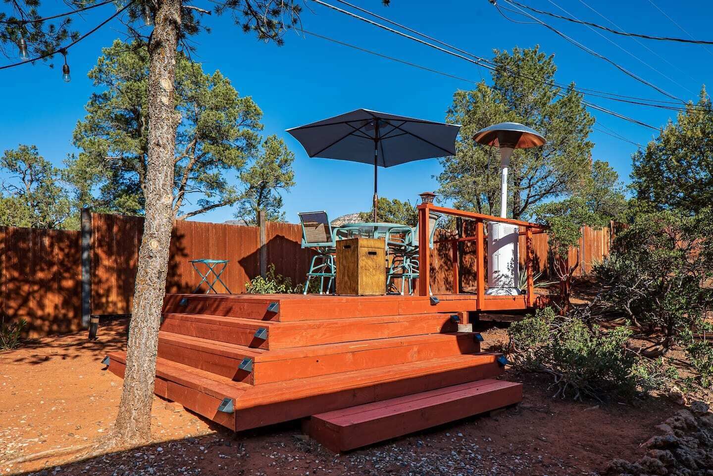 Una terraza de madera con escalones que conducen a una zona de estar cubierta, rodeada de árboles y una valla de madera.