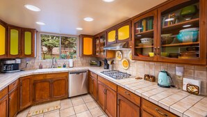 Une cuisine dotée de meubles en bois, d’un lave-vaisselle, d’une cuisinière et d’une fenêtre donnant sur un paysage verdoyant.
