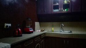 Une cuisine à la lumière tamisée, avec des meubles de rangement en bois, une bouilloire rouge, un mixeur et un évier.