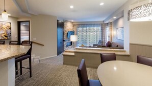 A modern hotel room with a dining area, a stone accent wall, and a view of the city. - Marriott Desert Springs II, Luxury 1 bedroom villa (Palm Desert)