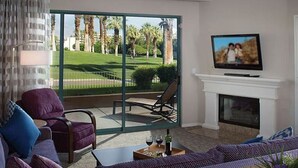 A living room with a sofa, a television, a fireplace, and a view of a golf course. - Marriott Desert Springs II, Luxury 1 bedroom villa (Palm Desert)