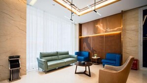 Un hall d’entrée moderne avec un canapé vert, deux fauteuils bleus, une table basse ronde et un mur décoratif en bois orné d’une plaque.