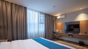 Une chambre d’hôtel avec un grand lit, un bureau avec une chaise, une télévision et une fenêtre avec des rideaux.