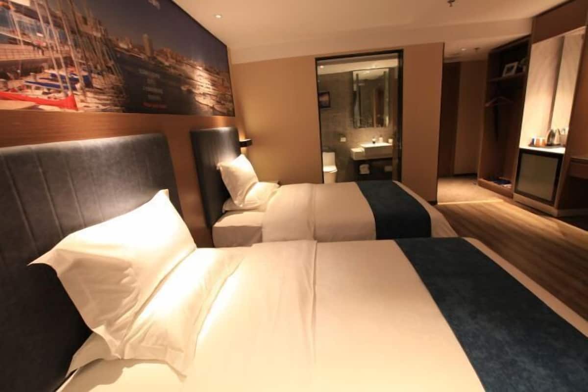 A hotel room with a large bed, a headboard, a nightstand, a mirror, a wardrobe, and a view of boats through a window.
