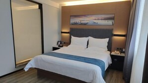 Una habitación de hotel con una cama grande, un cuadro sobre la cama y una mesita de noche con un teléfono y una lámpara.