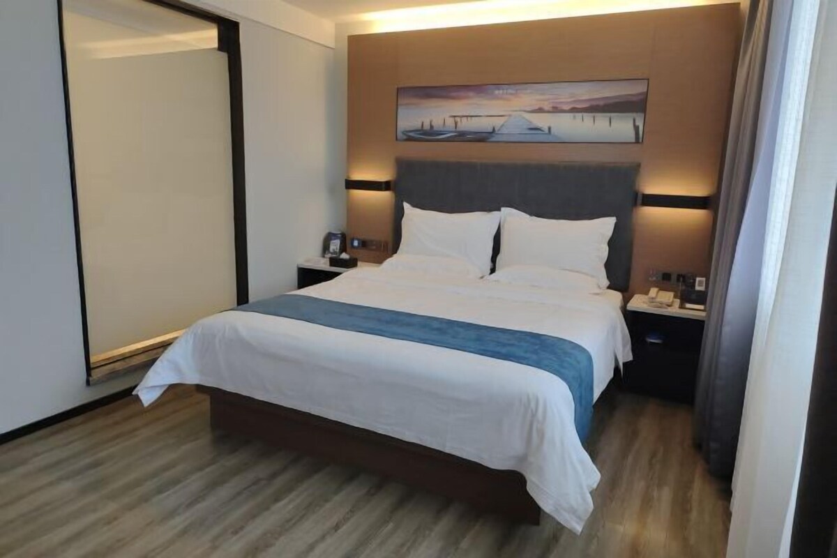 Una habitación de hotel con una cama grande, un cuadro sobre la cama y una mesita de noche con un teléfono y una lámpara.