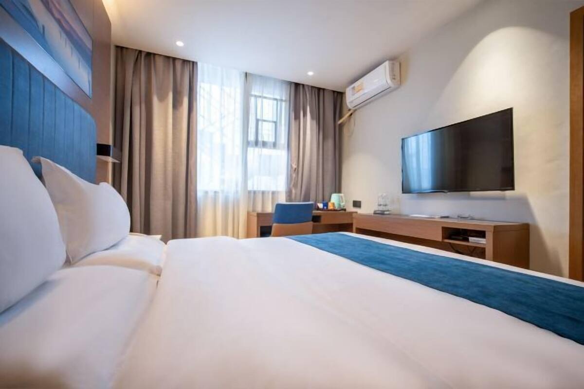 A hotel room with a large bed, a desk, a flat-screen TV, and a window with curtains.
