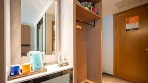 Habitación de hotel con cafetera, botellas de agua, un espejo, un estante con pantuflas y una puerta de madera.