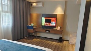 Habitación de hotel con cama, escritorio con computadora, televisión y ventana con cortinas.